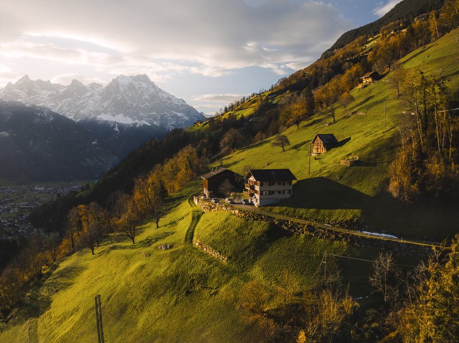 Aerial view of buildings on a steep alpine hillside with snow-capped peaks behind