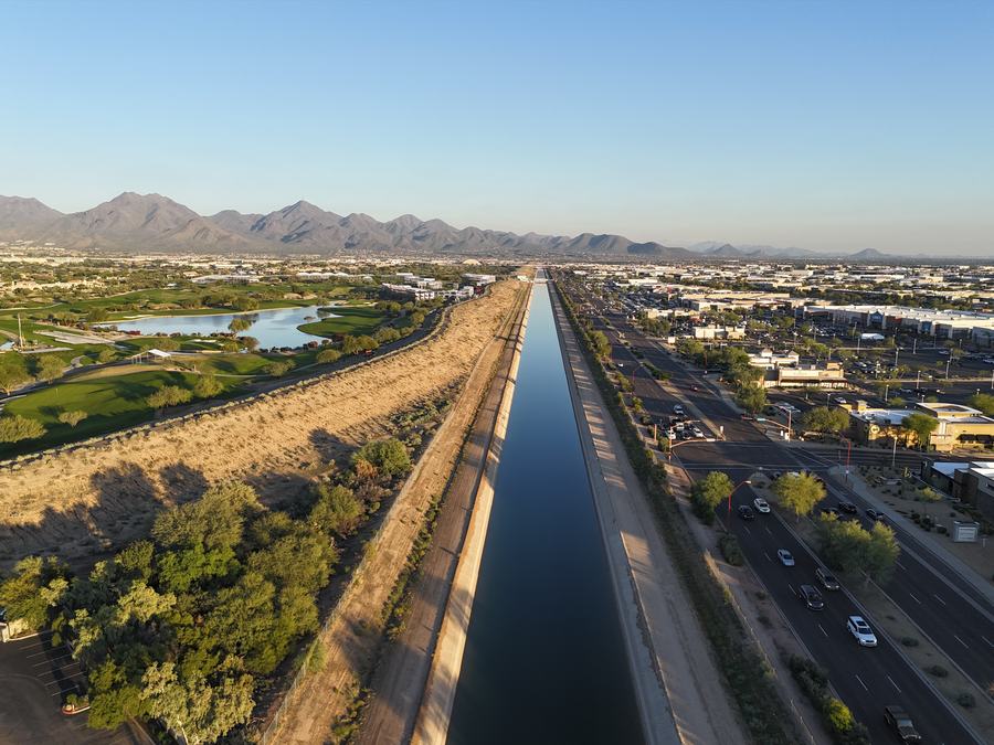 Aerial view along a canal separating a retail corridor from a golf course with mountains behind