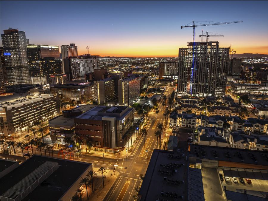 High-rise under construction with tower cranes lit at dusk over a downtown Arizona skyline