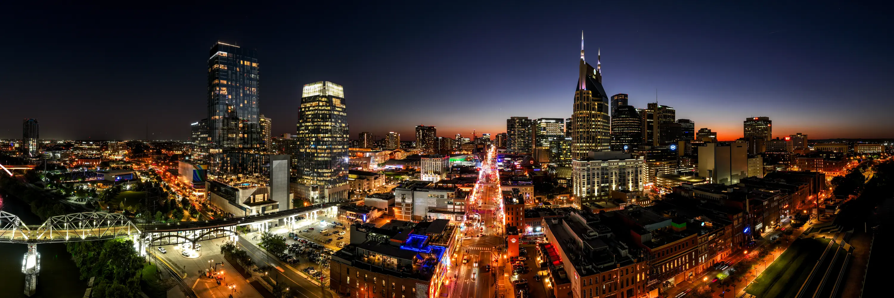 Wide panoramic aerial of a riverfront downtown skyline at blue hour